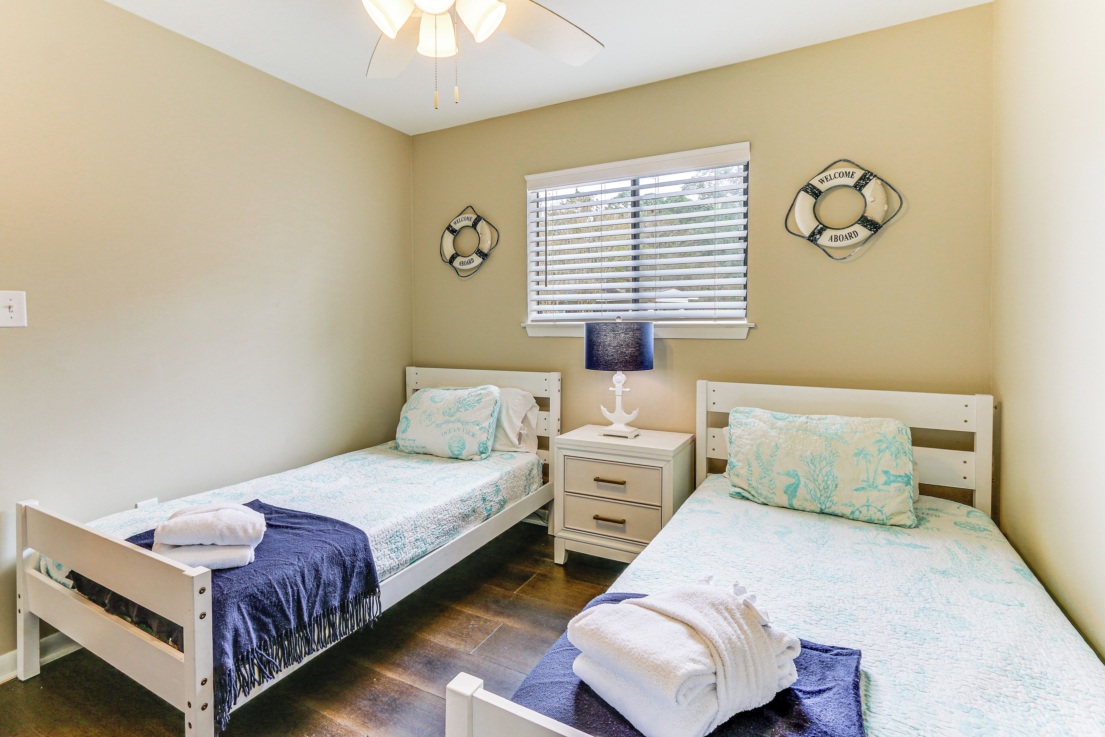 A bedroom with two single beds, a nightstand with a lamp, and a window with blinds.