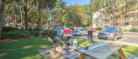 Un jardin avec un barbecue, une table de pique-nique et une voiture garée dans la rue.