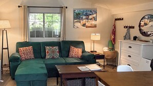 A green sofa with patterned cushions, a wooden coffee table, a white chair, a small side table with a lamp, and a dresser with a mirror. - Avalon Cottage < Half-mi to Beaches & Crescent Ave (Avalon)