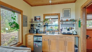 A compact kitchen with wooden cabinets, a built-in dishwasher, and a window overlooking a garden. - Yadkin River 'treehouse'~ Miles of Trails On-site (East Bend)