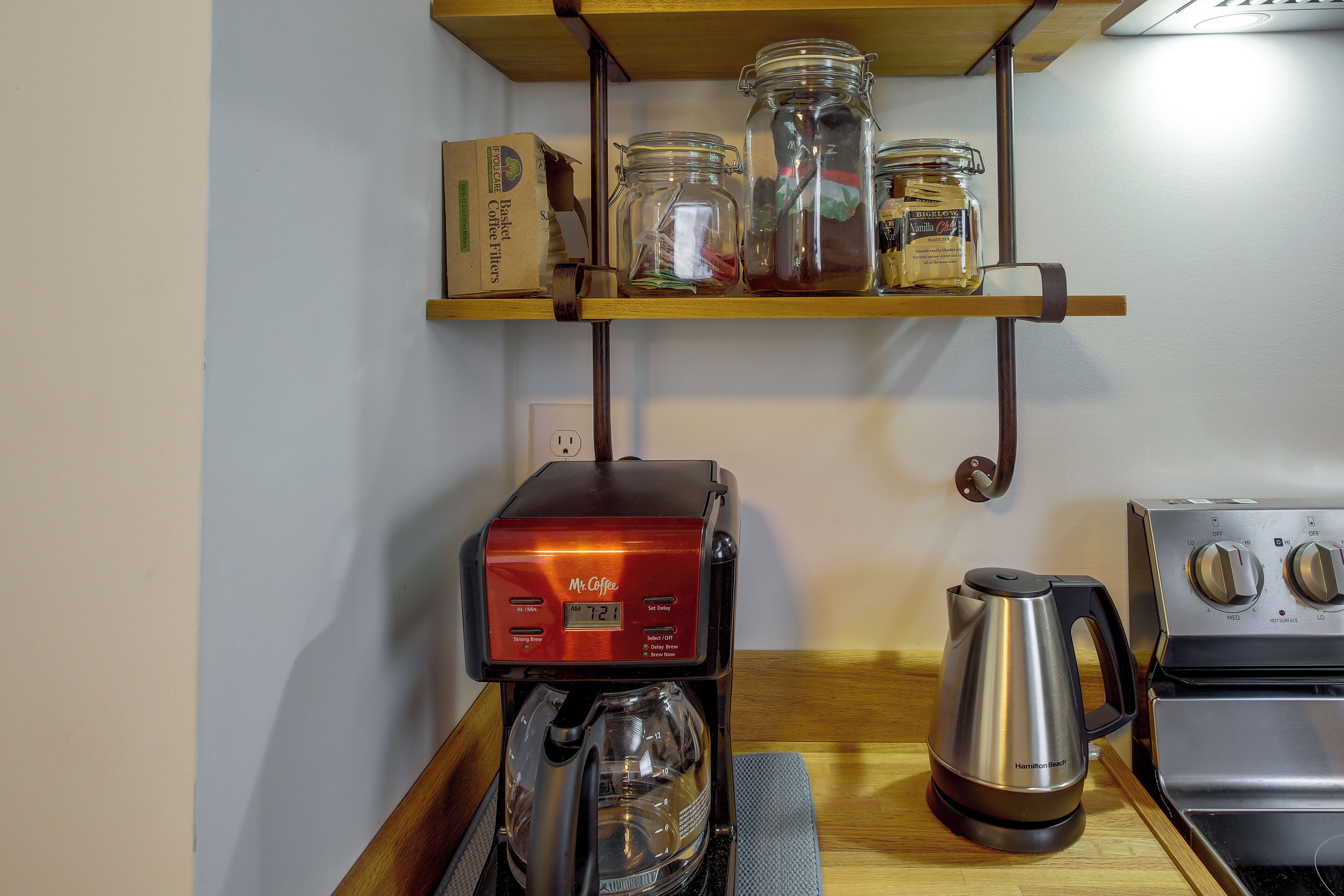 A kitchen with a coffee maker, a kettle, and jars on a shelf.