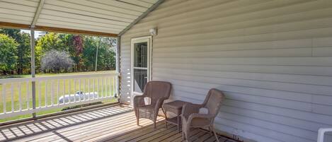 A covered porch with wooden flooring, two wicker chairs, and a small table.