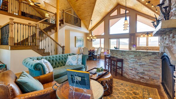 A spacious living area with a high ceiling, a fireplace, a staircase, and a view of the outdoors. - Hot Tub & Fire Pit: Idyllic Getaway in Angel Fire! (Angel Fire)