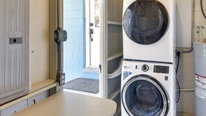 Une buanderie équipée de machines à laver et de sèche-linge superposés, une porte donnant sur l’extérieur et une petite fenêtre.