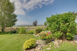 Un jardín bien cuidado con diversas plantas y flores, una valla de madera y una vista despejada del campo.