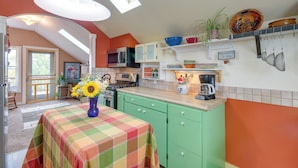 A kitchen with green cabinets, a microwave, a stove, and a coffee maker. There is a window with a view of trees and a door leading to another room. - Charming Livingston Vacation Rental w/ Views! (Livingston)