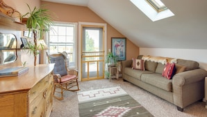 A cozy attic room with a sloped ceiling, a large window, a sofa, a rocking chair, and a wooden dresser. - Charming Livingston Vacation Rental w/ Views! (Livingston)