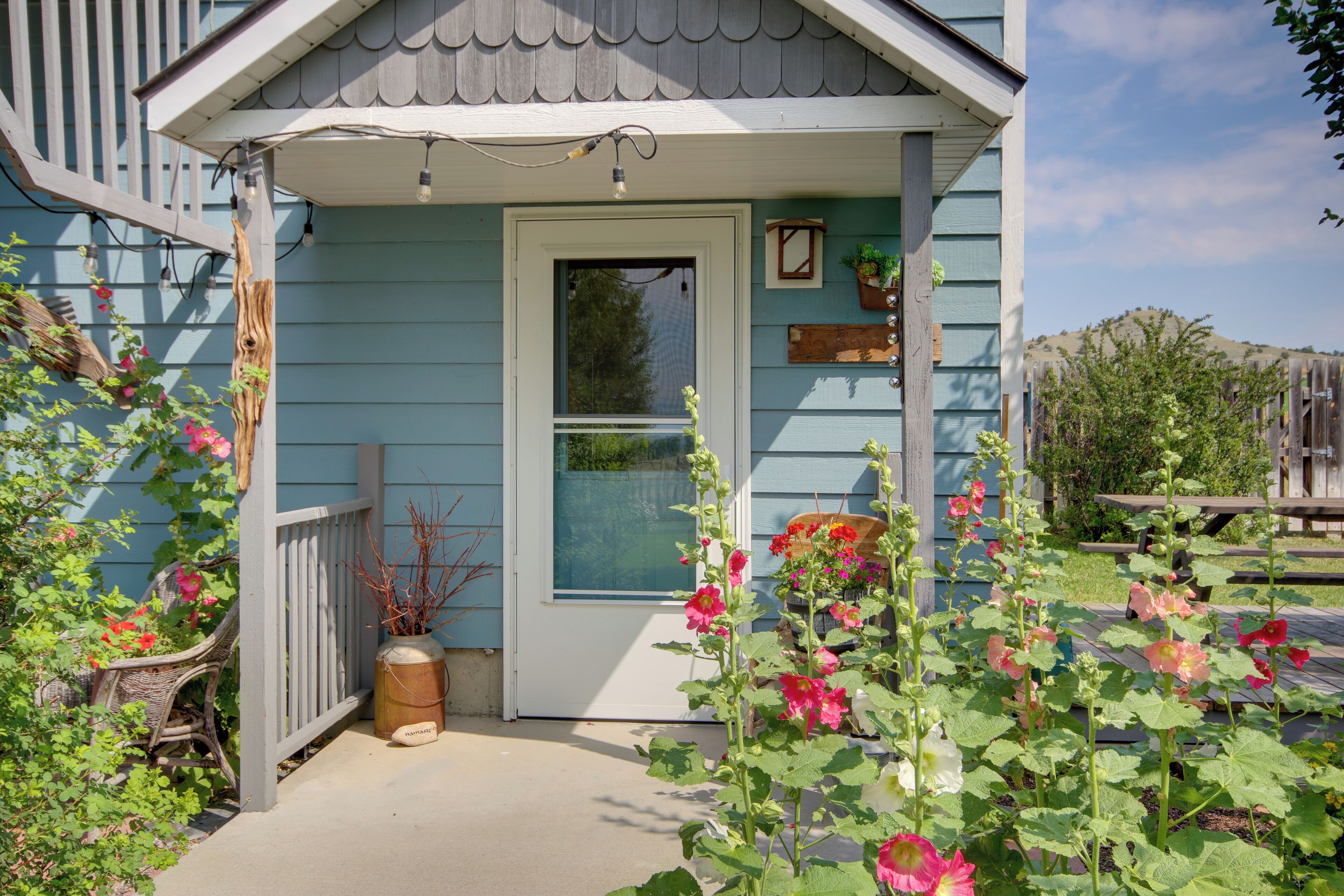 A house with a porch, a door, and a window. There are plants and flowers around the porch.
