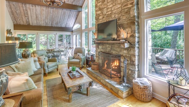A spacious living room with a stone fireplace, comfortable seating, and large windows offering a view of the outdoors.