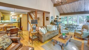A spacious living area with a wooden ceiling, a sofa set, a coffee table, and a dining area with chairs and a table.