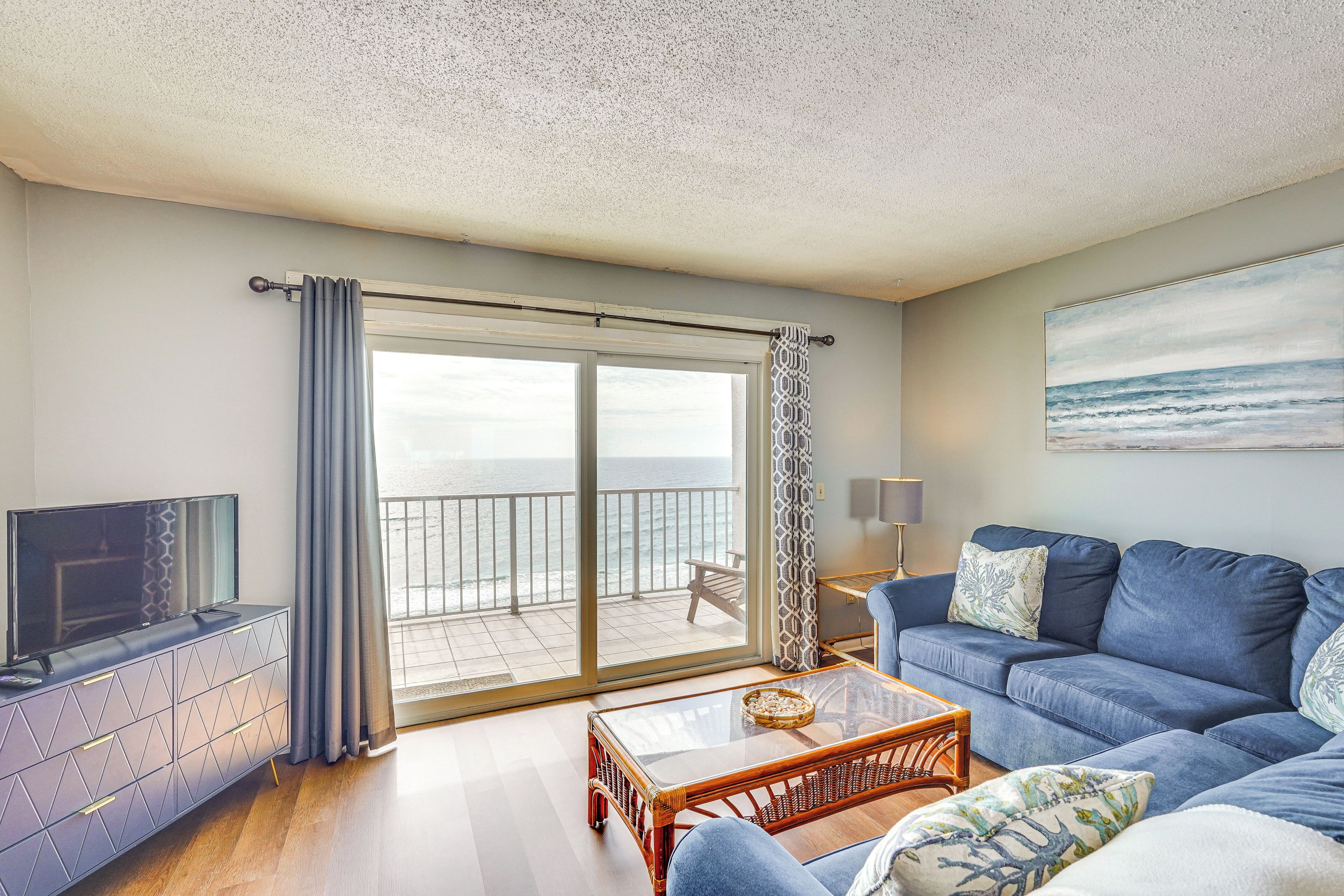 Een woonkamer met een televisie, bank, salontafel en een balkon met uitzicht op zee.