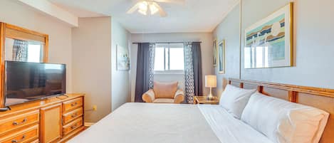 Una habitación de hotel con una cama grande, tocador de madera, televisor y ventilador de techo.