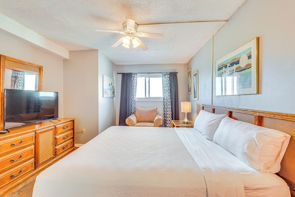 A hotel room with a large bed, wooden dresser, television, and ceiling fan.