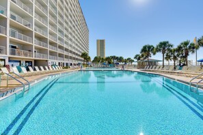 Uma área de piscina de hotel com espreguiçadeiras e um edifício grande com varandas.