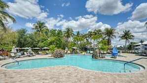 A swimming pool with lounge chairs and umbrellas, surrounded by palm trees and a clear sky. - Newly Updated Golf Villa w/ Free Golf May-oct (Naples)