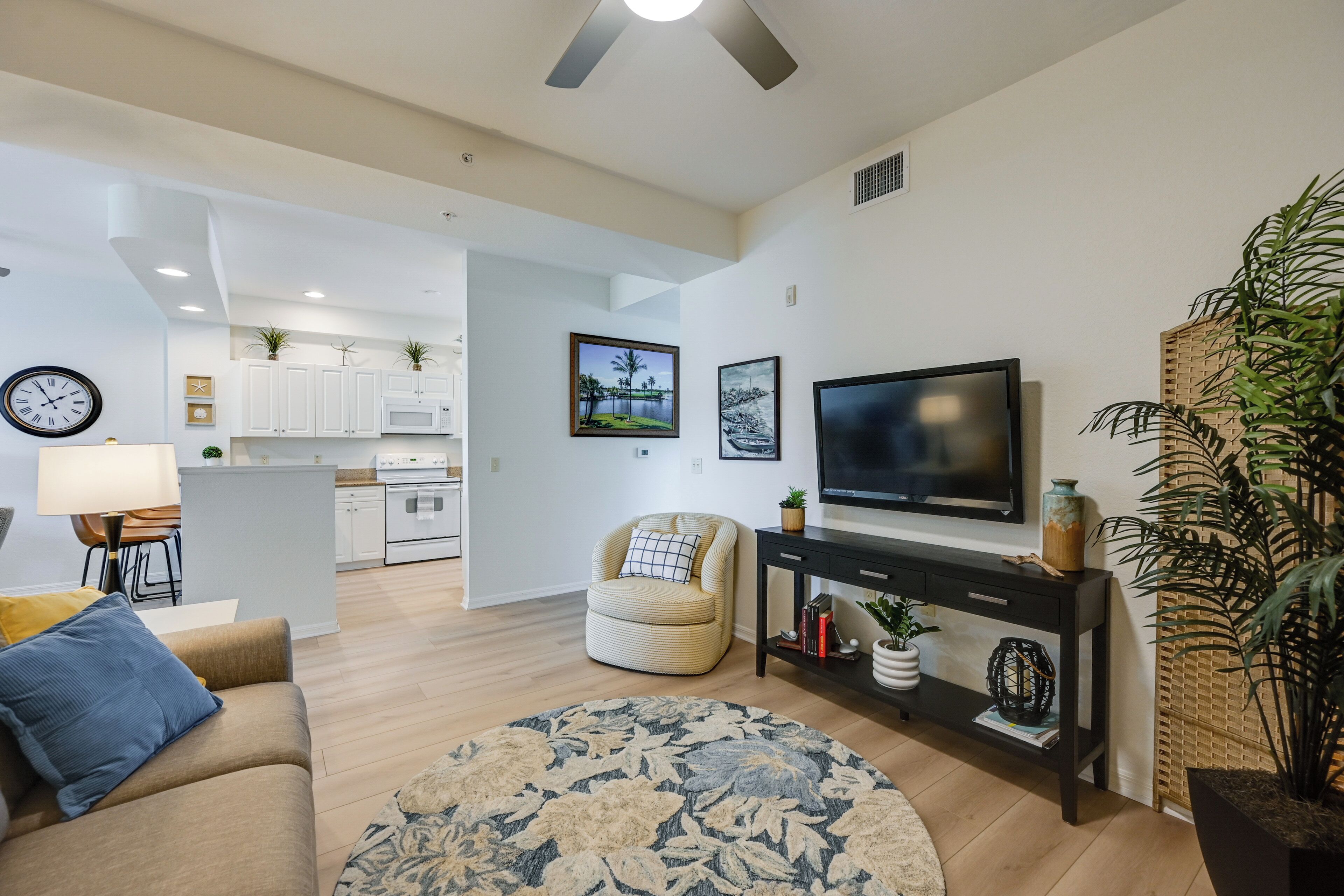 A modern living room with a sofa, a coffee table, a TV, and a dining area with a kitchen in the background.