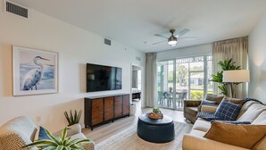 A modern living room with a flat-screen TV, comfortable seating, a ceiling fan, and a view to the outside. - Newly Updated Golf Villa w/ Free Golf May-oct (Naples)
