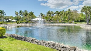 A pond with a fountain, surrounded by palm trees and a building with a white roof. - Newly Updated Golf Villa w/ Free Golf May-oct (Naples)