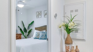 A bedroom with a bed, a ceiling fan, a nightstand, a vase with flowers, and a wall-mounted light fixture. - Swim, Tour & Explore! Gulf Shores Condo w/ Balcony (Gulf Shores)