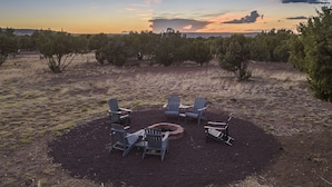 An outdoor seating area with Adirondack chairs and a fire pit, surrounded by sparse vegetation and a clear sky. - Family Reunions, Groups, 40 acres wide open spaces (Concho)