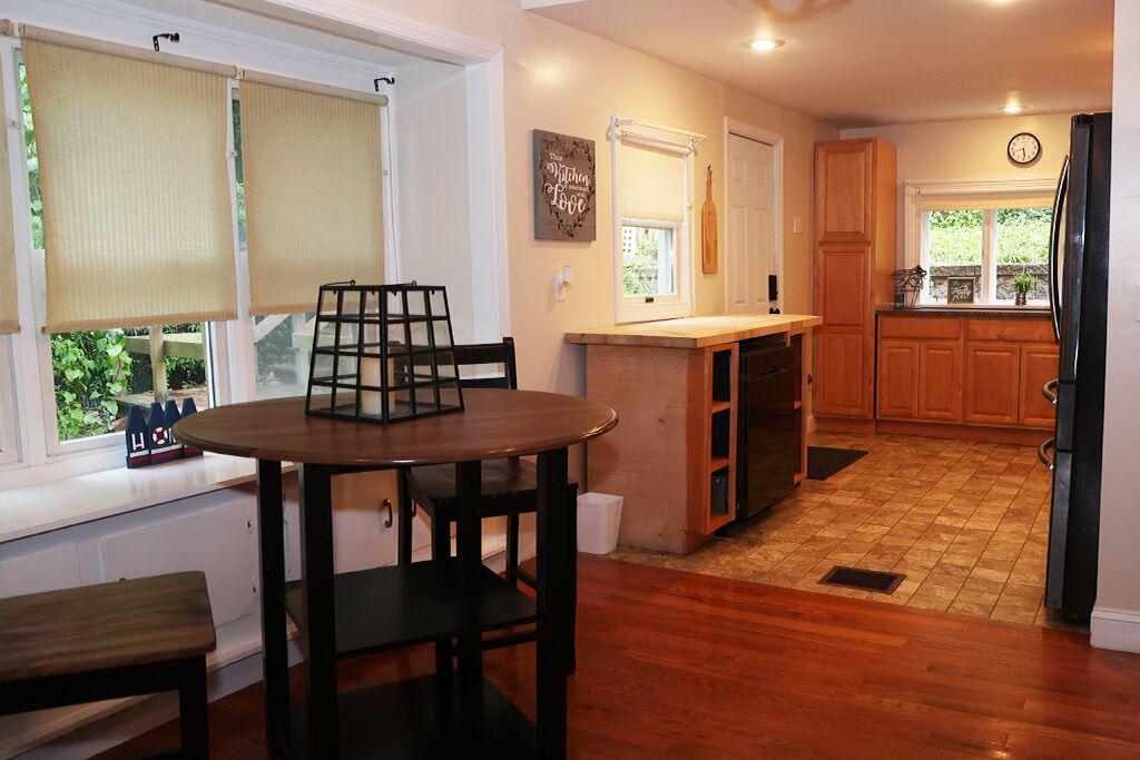 A kitchen with wooden cabinets, a black refrigerator, and a dining area with a round table and chairs.