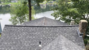 A house with a grey shingled roof, a stone chimney, and a small window. - Serene 2-bedroom, 2-bath lakefront retreat on scenic Staffordville Lake (Stafford)