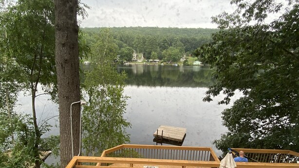 A wooden deck with outdoor furniture, overlooking a lake with boats and houses in the background. - Serene 2-bedroom, 2-bath lakefront retreat on scenic Staffordville Lake (Stafford)