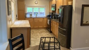 A modern kitchen with wooden cabinets, a black refrigerator, and a dining table with chairs. - Serene 2-bedroom, 2-bath lakefront retreat on scenic Staffordville Lake (Stafford)