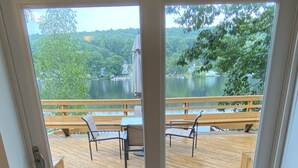 A view from a room with a sliding glass door to an outdoor deck with wooden flooring, a table, chairs, and a bench. - Serene 2-bedroom, 2-bath lakefront retreat on scenic Staffordville Lake (Stafford)