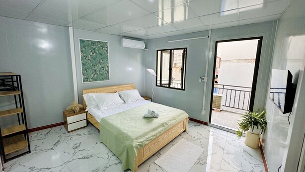 A bedroom with a bed, a nightstand, a wall-mounted TV, a window, and a balcony.
