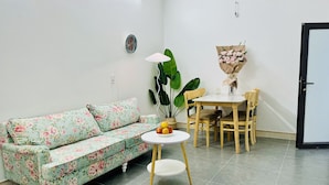 A living room with a floral sofa, a round table with chairs, a potted plant, and a bouquet of flowers.