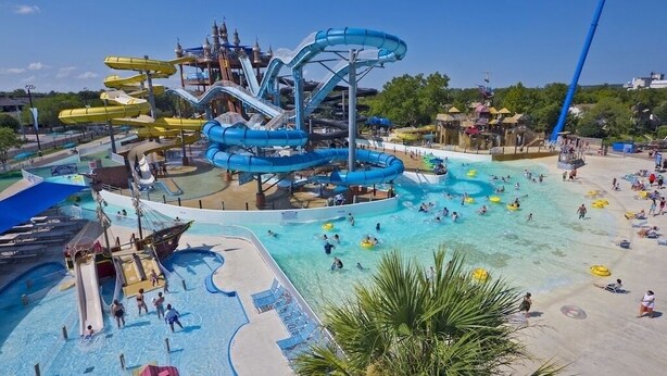 Un parque acuático con múltiples toboganes y piscinas, incluyendo un gran tobogán central y piscinas más pequeñas para nadar y disfrutar de actividades acuáticas.