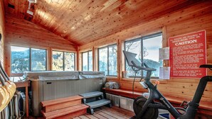 Una cabaña de madera con sauna, bicicleta estática y grandes ventanales con vistas a las montañas.