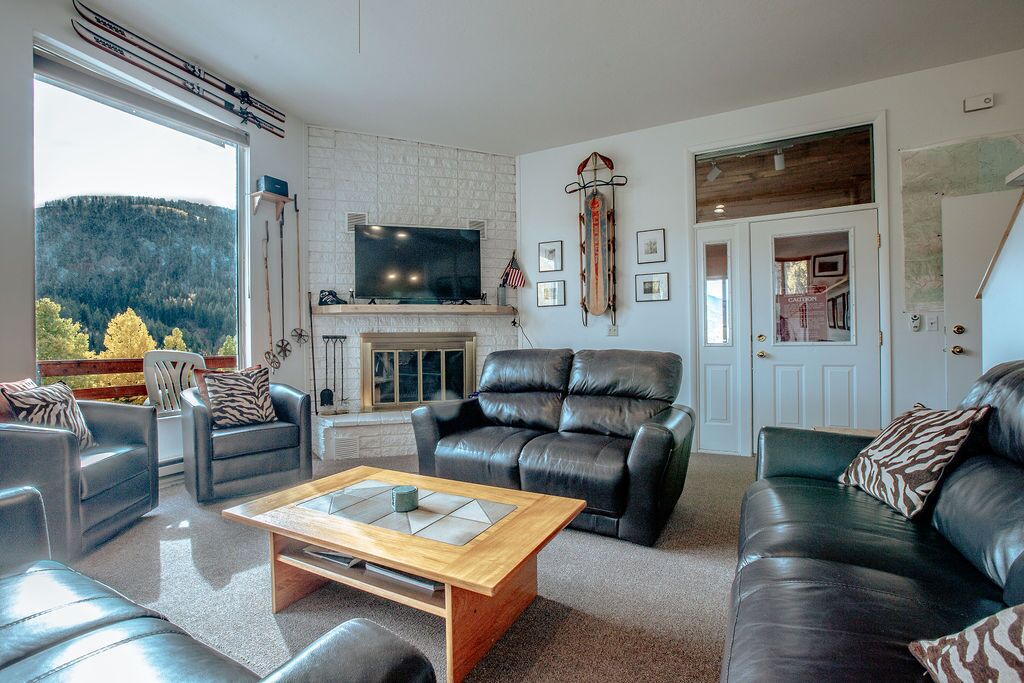 A modern living room with leather sofas, a fireplace, a television, and a view of a forested area.