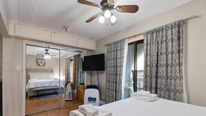 A hotel room with a bed, a ceiling fan, a television, a heater, and a large mirror. - Cozy Studio Loft | Indoor Pool & Walk to Beach (Corpus Christi)