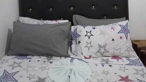 A bed with a tufted headboard, grey and white pillows, and a bedspread with star patterns.