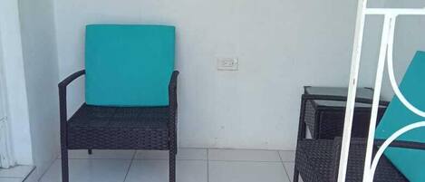 Un pequeño espacio al aire libre con dos sillas de mimbre, un felpudo y una ventana con vistas al exterior.