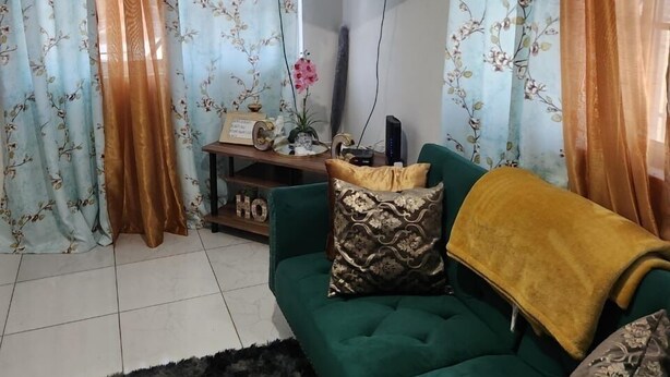 A living room with a green sofa, a flat-screen TV, and floral curtains.