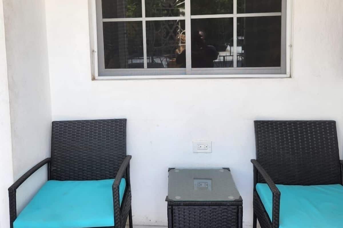 Une pièce avec deux fauteuils en osier et une petite table, une grande fenêtre et un mur blanc.