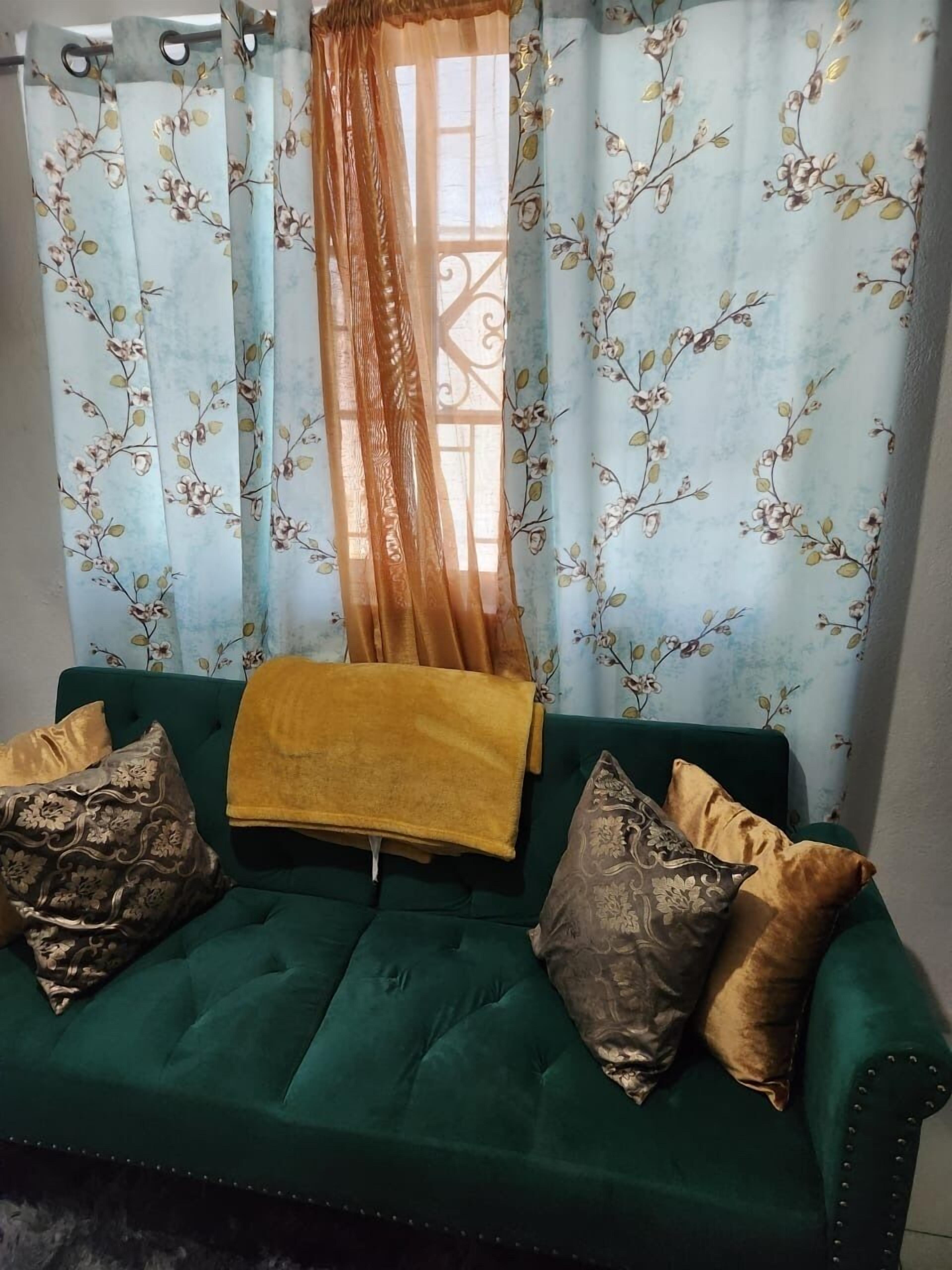 Un sofá verde con cojines estampados y una manta amarilla.