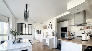 A modern kitchen with white cabinets, a wooden countertop, and a dining area with a white table and black chairs. - Appartement de Charme Hypercentre Brest (Brest)