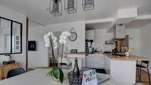 A modern kitchen with white cabinets, a wooden countertop, and a built-in oven. There is a dining area with a table, chairs, and a vase with white orchids. - Appartement de Charme Hypercentre Brest (Brest)