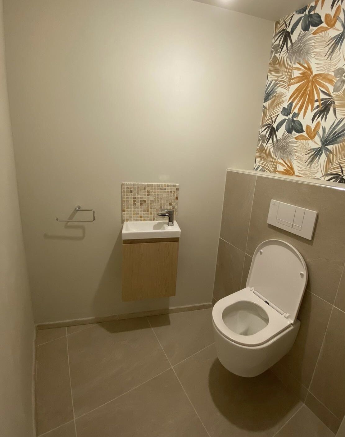 Een badkamer met toilet, wastafel met betegelde spatwand en lichtschakelaar aan de muur.