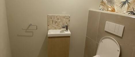 Een badkamer met toilet, wastafel met betegelde spatwand en lichtschakelaar aan de muur.