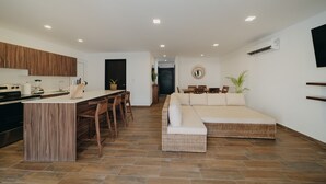 Una cocina moderna con una isla central, comedor con sillas, sofá y televisor montado en la pared.