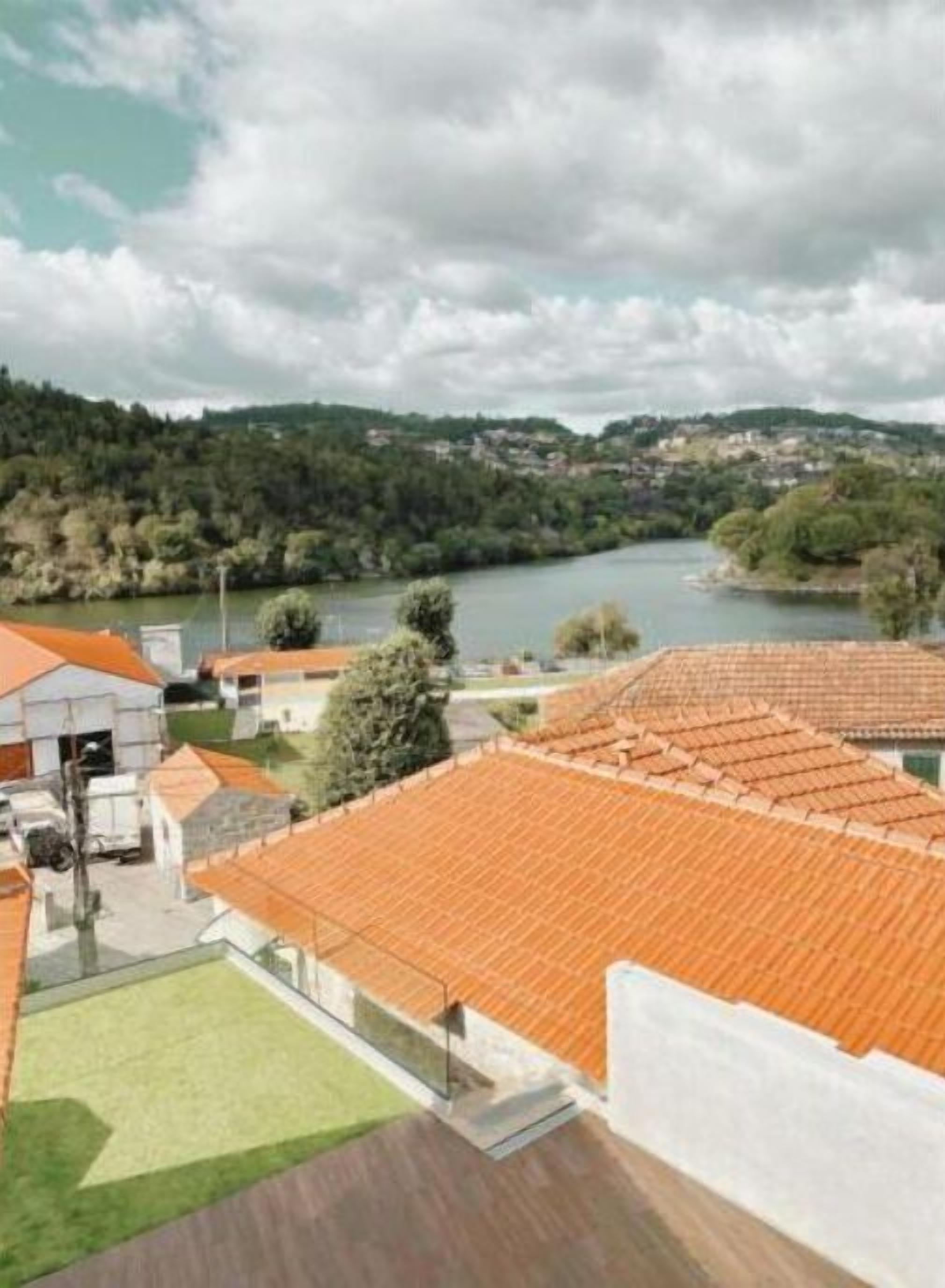 A residential area with terracotta-tiled roofs, a grassy lawn, and a river in the background.