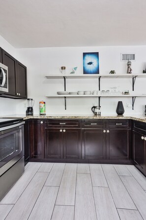 A modern kitchen with dark cabinetry, a white countertop, and a granite backsplash.