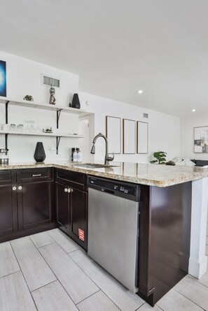 A modern kitchen with dark cabinetry, a dishwasher, and a granite countertop.