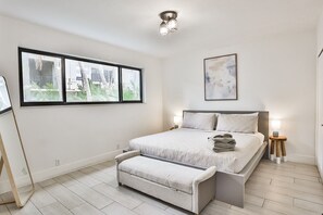 A bedroom with a bed, bedside tables, a bench, a window, and a ceiling light fixture.