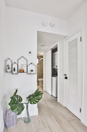 Ein Flur mit einer weißen Tür, einer weißen Wand mit gerahmten Bildern und einem Blumentopf.